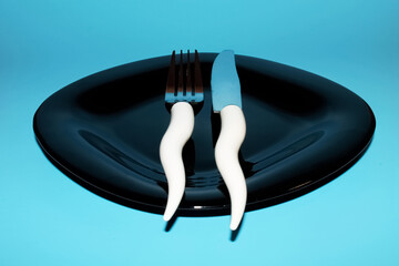 Etiquette fork and knife on a glossy black plate on a blue isolated background