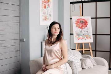 A pregnant woman is sitting on the couch in her pajamas at home