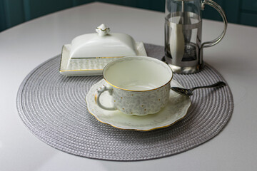 A white tea cup with a golden pattern , a carnival and a silver teapot on a white table