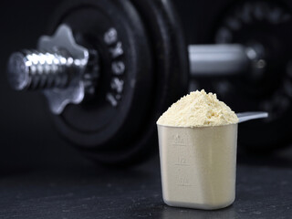 whey protein powder in scoop with dumbbell on black background