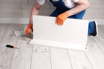 master in overalls assembles a white furniture box in an apartment