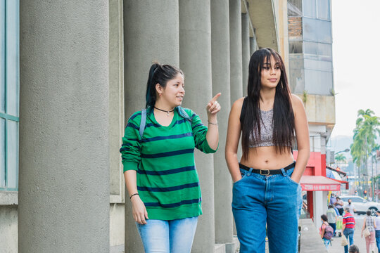 two beautiful latina girls (caucasian and brunette) walking down the street, happily talking and pointing out things they would like to buy. college girls taking a stroll through the city.
