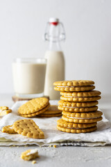 Shortbread cookies with creamy filling on a light napkin. A glass and a bottle of milk in the background. White background