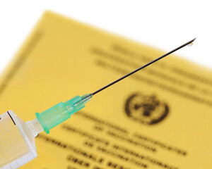 medical syringe filled with vaccine and yellow international vaccination certificate on white background, close up of a vaccination needle