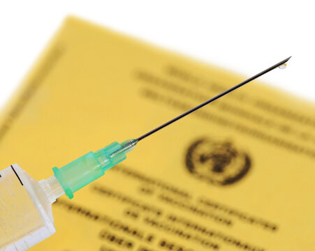 medical syringe filled with vaccine and yellow international vaccination certificate on white background, close up of a vaccination needle