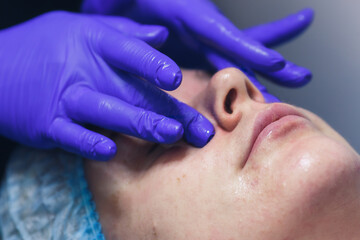 Fototapeta premium Facial skin care. Masseur's hands in gloves. Facial massage in beauty spa. Skin moisturizing treatment