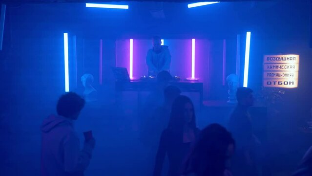 A crowd of people leaves the dance floor of a nightclub under the light of colored spotlights. One guy stays to dance. Night club