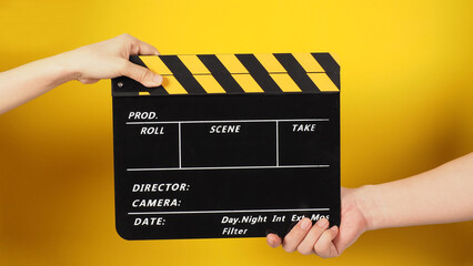 Two hands send and hold a Black clapper board or movie slate on yellow background.