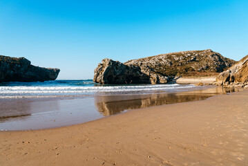 Beach of Cuevas del Mar, Caves of the sea, Llanes, Asturias, Spain. Long exposure, sunny day with bright blue sky