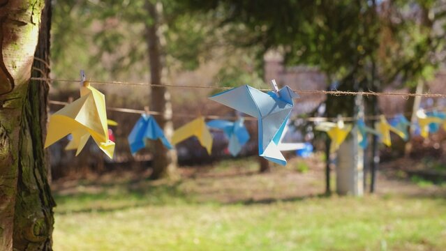 Blue and Yellow Origami Paper Peace Doves Decoration Hanging in Park as Sign of Support to Ukraine during War with Russia after Invasion - Powered by Adobe