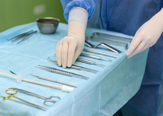 Surgical instruments in the operating room. A nurse in a surgical suit and gloves is preparing for a tooth implant operation.
Dental probe, tweezers, scalpel, needle holder, rasps on instrument table.