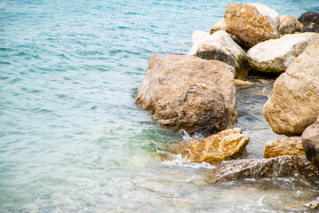 stone beach washes the sea. The sea is clear blue. Background of stone shore by the sea.