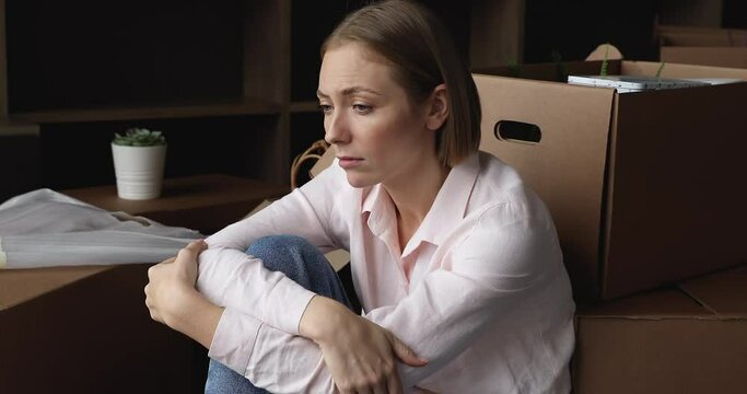 Unhappy exhausted young woman sit on floor near carton boxes with stuff, looks tired due long relocation, feeling desperate due lender repossess home, bank take house due loan debt, divorce concept