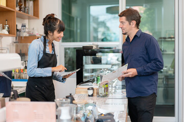 Female barista owner in apron smiling and using tablet ordering from customer in coffee shop