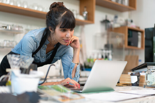 Beautiful female barista owner in apron checking online order from customer on computer tablet at coffee.Small business concept