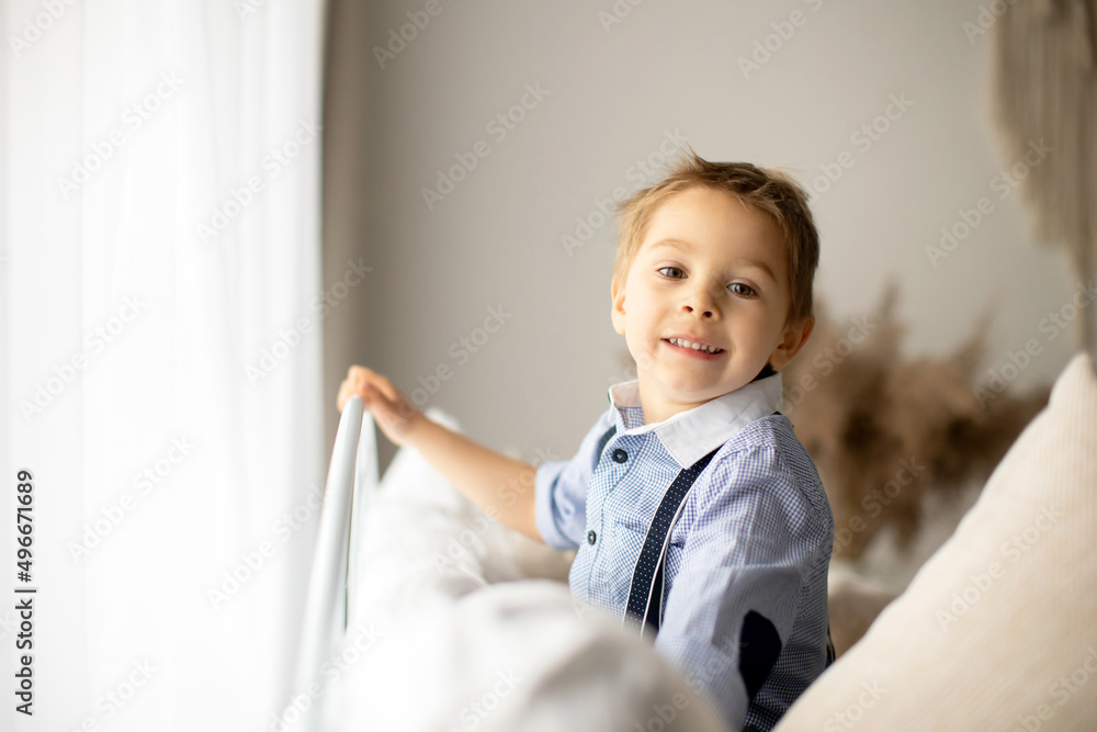 Wall mural Beautiful fashion preschool child, boy, having fun at home in bed, looking out of the window