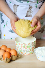 A woman in an apron with an Easter bunny print prepares dough for cakes and puts it in baking pans....