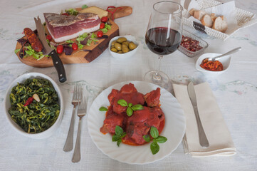 Italian cuisine: meat stew (ragù napoletano) with basil, broccoli, speck, salami, olives, bread, chilli sauce and red wine.
