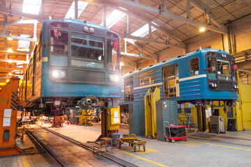 Passenger locomotives of the underground metro raised on jacks with headlights on in the depot,...