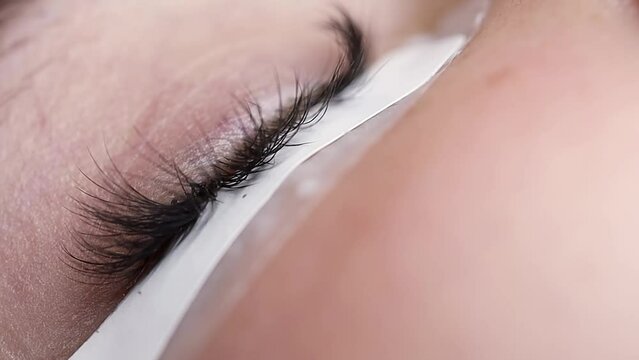 close-up eyelash extension procedure master using tweezers sticks a bunch of eyelashes