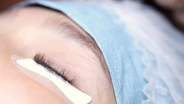 an eyelash extensionist performs a Masten procedure holding tweezers in his hands and gluing bunches of cilia with them