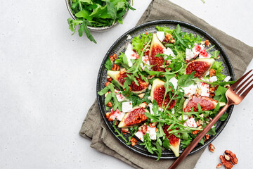 Delicious summer salad with sweet  figs, white feta cheese, walnuts, arugula and jam vinegar dressing on white table background, top view, negative space