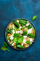 Delicious summer salad with pear, grapes, roquefort cheese, spinach, walnuts on blue table background, top view, negative space