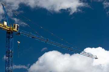 Industrial crane on a construction site against blue sky with white clouds. Residential flat buildings under construction.
