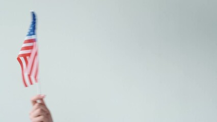 USA flag. Independence day. Embassy consulate. Female hand waving American national symbol with red white stripes 50 stars on blue isolated on light neutral copy space background.