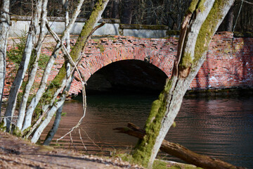 Czerwony, ceglany most nad rzeką. Stara przedwojenna budowla pokryta mchem. Słoneczny dzień,...