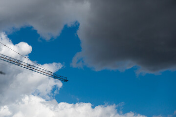 Industrial crane on a construction site against blue sky with white clouds. Residential flat buildings under construction.