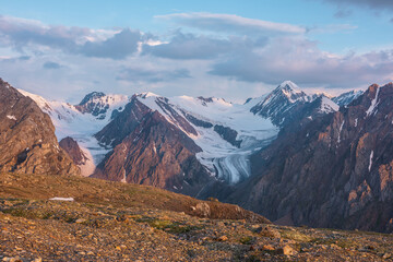 Vivid alpine landscape with high snow mountains and large glacier in sunrise colors. Colorful mountain scenery with sunlit golden rocks and mountains at sunrise. Early morning at very high altitude.