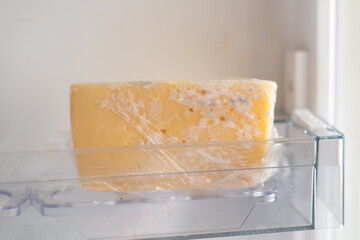 Moldy cheese wrapped in cling film in the refrigerator. Incorrect storage, spoiled product, expired...
