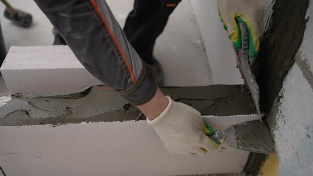 A builder lays aerated concrete blocks at a construction site. High-quality laying of blocks on glue, building a house. A worker glues blocks, builds a wall.