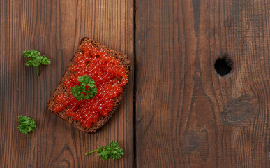 red salmon caviar lies on a piece of rye bread. Brown wooden table