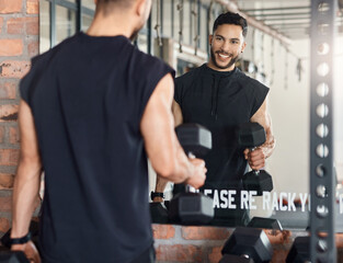 Workout to impress yourself. Shot of a sporty young man looking at himself in a mirror while exercising with dumbbells in a gym. - obrazy, fototapety, plakaty