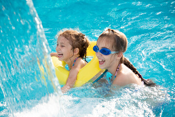 Two young smiling girls in a swimsuit bathes play in a pool with blue clear water in blue swimming...