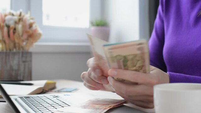 Against the background of a table with a laptop, female hands leaf through Russian banknotes with a face value of 5000 and 2000 rubles, the concept of a family budget