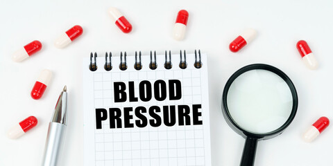 On a white surface are tablets, a pen, a magnifying glass and a notepad with the inscription - BLOOD PRESSURE