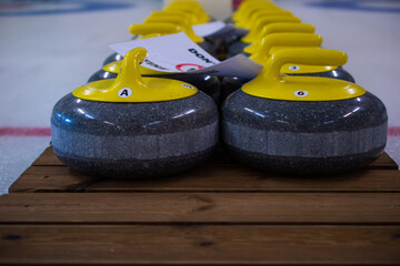 Curling stones with a yellow handle sit on a wooden base.