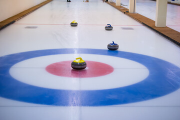 A yellow-handled curling stone sits on the ice in the center of the house, with the other stones...