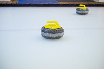 Close-up of a curling stone with a yellow handle stands on ice.