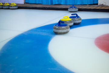 A yellow-handled stone stands between two blue-handled curling stones on the blue circle of the...