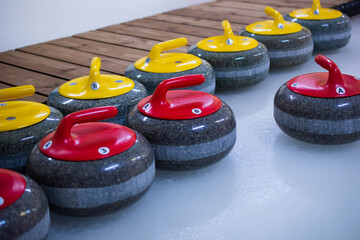 There are curling stones with red and yellow handles on the ice. The stones are ready to play.