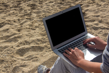 Side view of young woman sitting on beach and typing on laptop, work from anywhere, freelance travel on holiday summer.