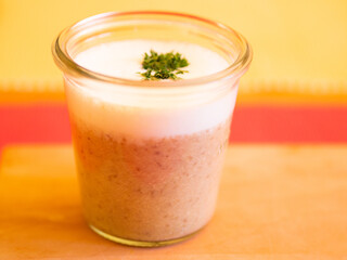 Champignon cappucino with milk froth and parsley, served in a glass on a wooden board