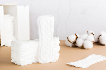 Fototapeta na wymiar Clean disposable sanitary pads in a stack and in a box and a branch of cotton on a beige background. Women's health and comfort concept
