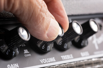 hand turning up the volume of a guitar amplifier, treble and bass control knobs out of focus ,...