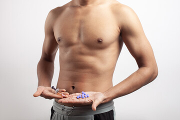 shirtless fitness muscular man holding anabolic steroid syringe and multivitamin supplement pills on palm