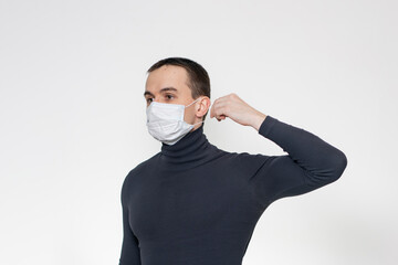 A young man puts on medical blue mask. Confident calm guy  with disposable mask. White background.
